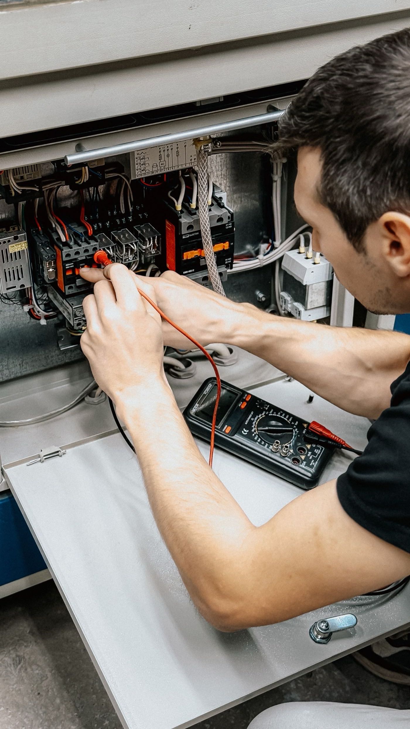 Electrician testing circuits in a panel with a multimeter during an inspection